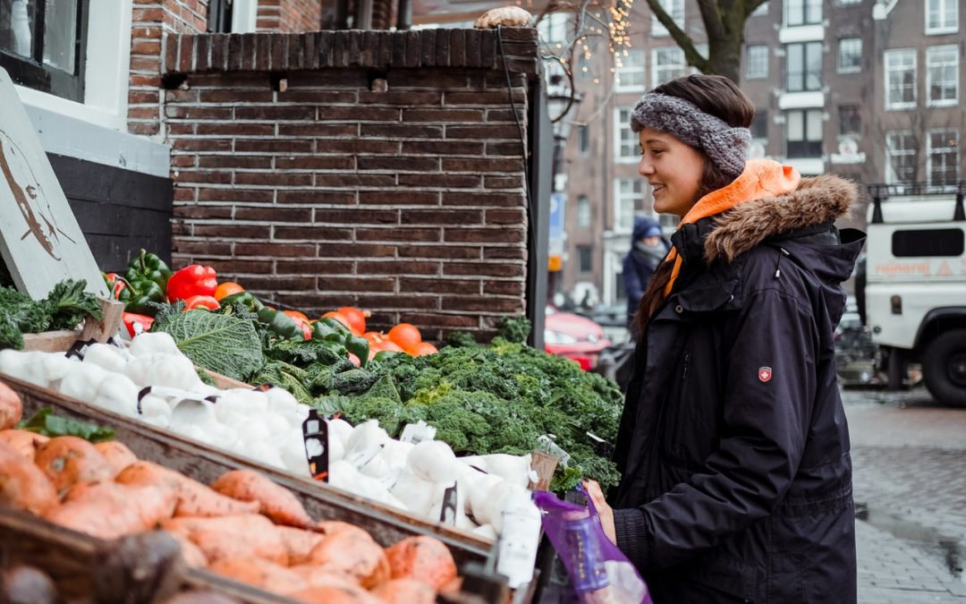 Alimenti riscaldanti in inverno | Donna in città sul marcipiede di fronte a casse di frutta e verdura